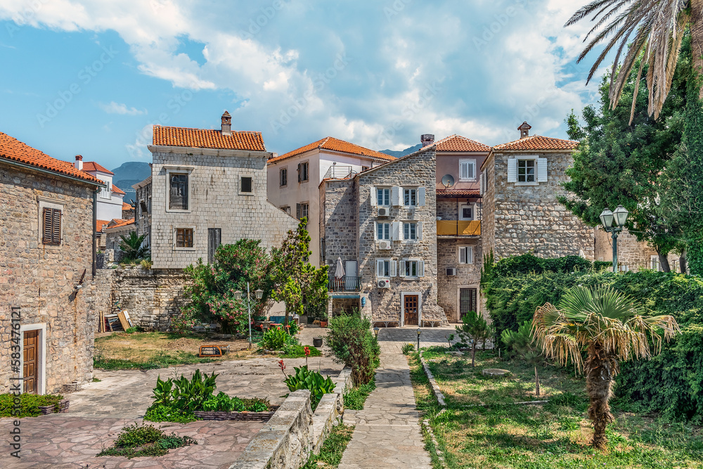 Ancient stone houses with red tiled roofs among the garden in the Old Town Stari Grad of Budva, Montenegro. Beautiful tourist architectural landscape