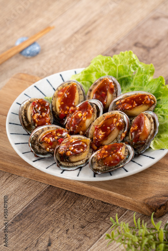 Delicious steamed abalone with Taiwanese five flavor sauce on wooden table background.