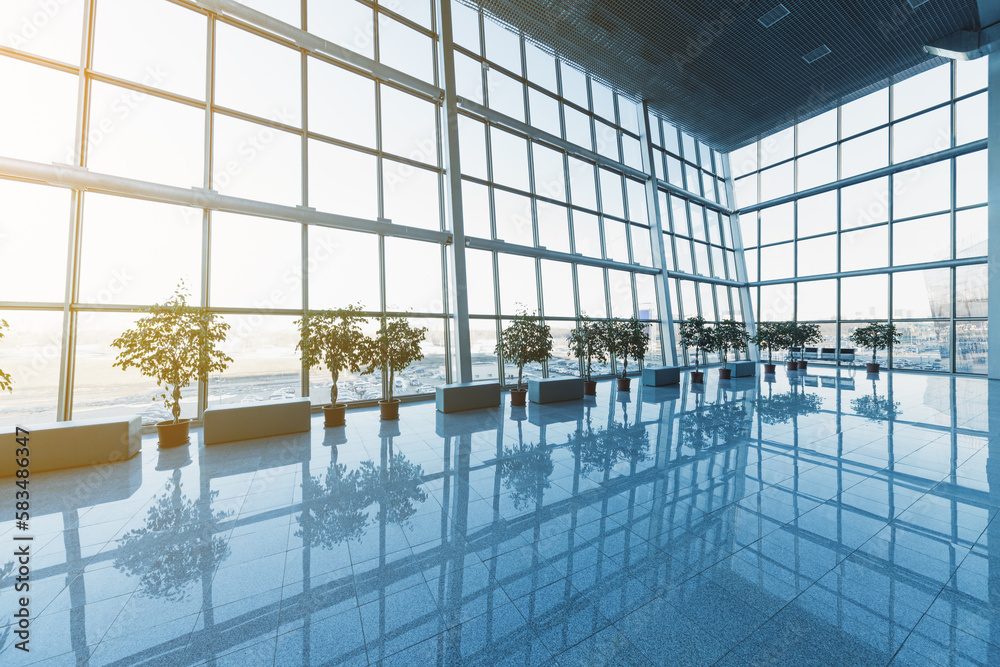 Interior of the modern lobby, terminal or waiting room with glass walls and reflective floor, natural light and flare