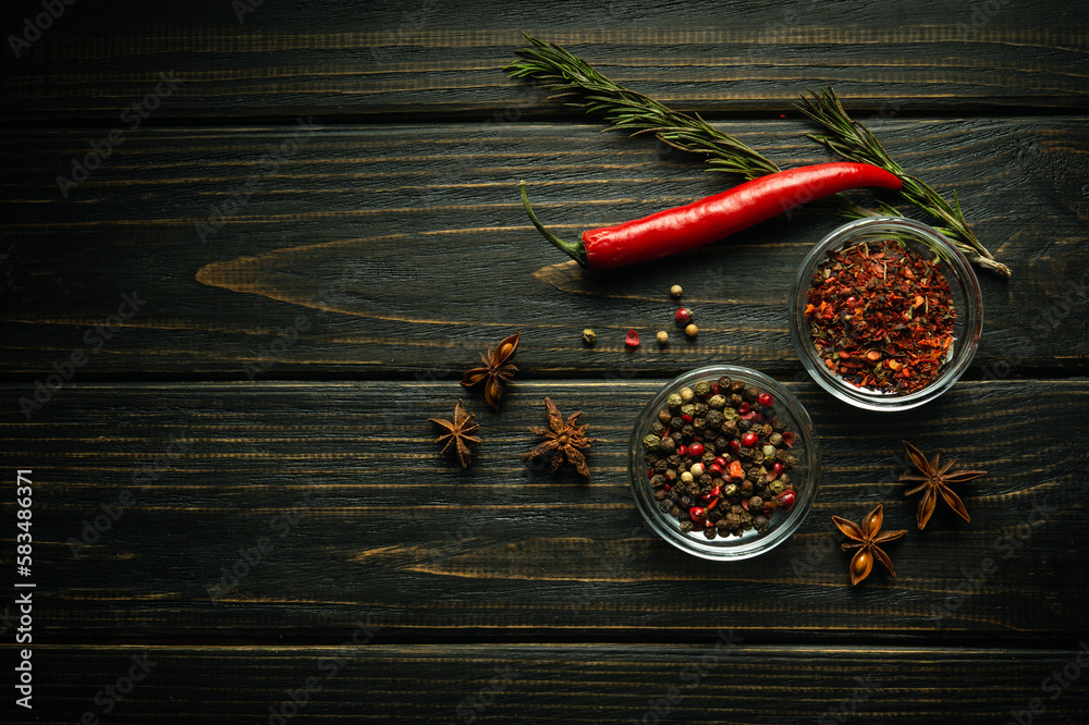 A set of peppers for adding to food and dry spices. Red chili pepper pods and dry star anise on black vintage kitchen table - obrazy, fototapety, plakaty 