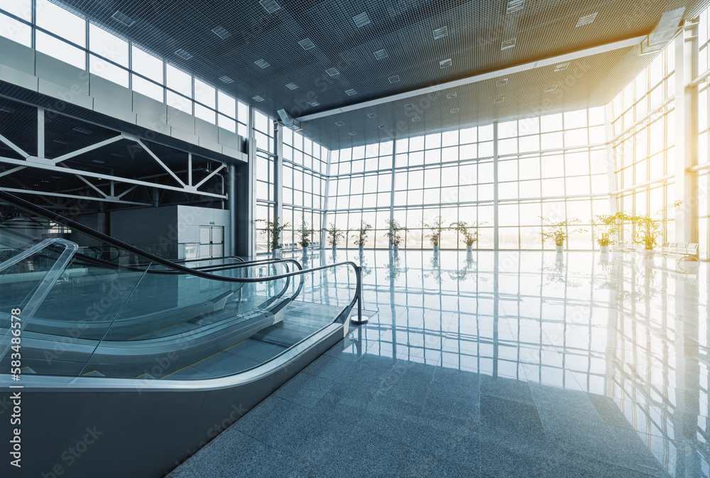 Escalator in lobby of modern office building, glass walls and reflective floor, natural light and flare