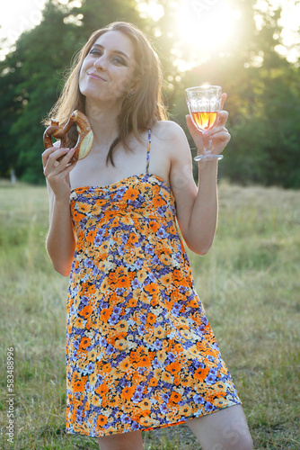 Obraz na płótnie Beautiful young woman in nature is wearing summer dress, drinking wine and eating a pretzel w salonie