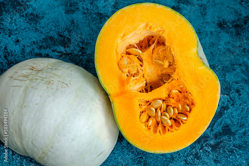 ripe orange pumpkin close-up cut into halves and seeds inside on a blue background, ripe healthy vitamin dietary vegetable,