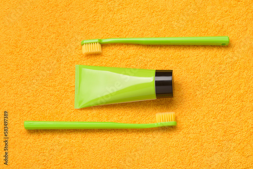 Green toothbrushes with paste tube on yellow bath towel. Oral hygiene products.