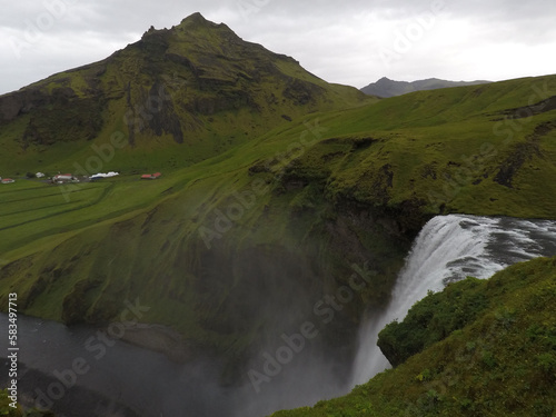 Scenic view of a waterfall and a green meadow under a gray sky in Iceland