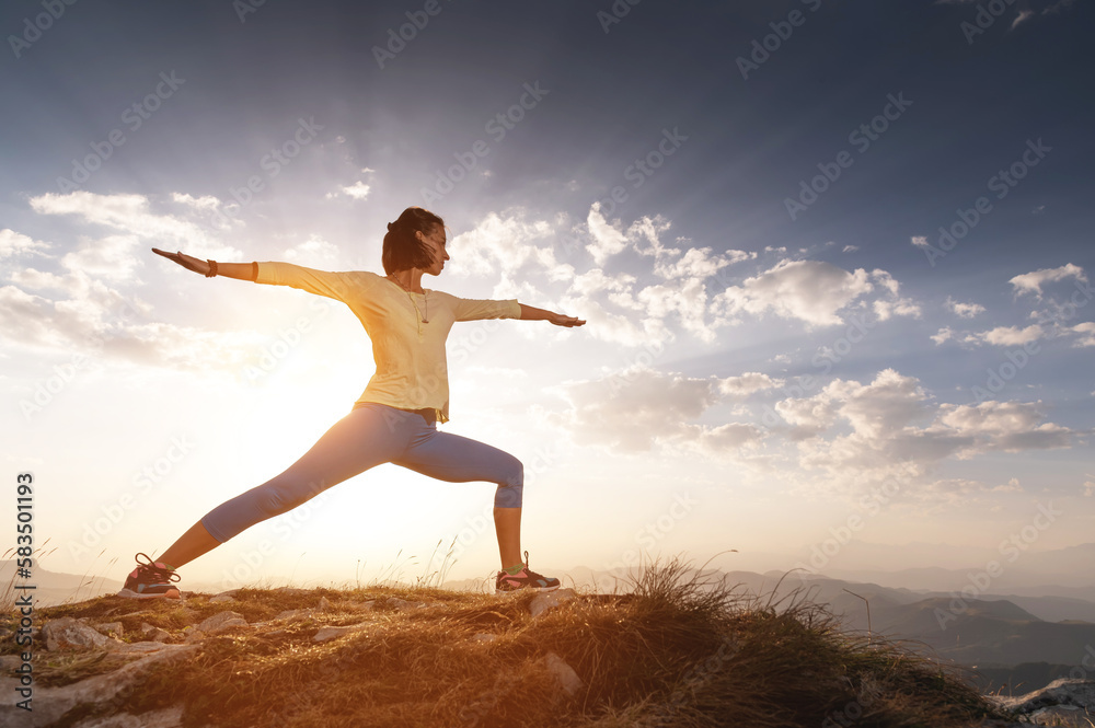 young woman practices yoga and fitness outdoors in a beautiful mountain landscape. Morning dawn, warrior pose young woman practices yoga and fitness outdoors in a beautiful mountain landscape. Morning dawn, warrior pose