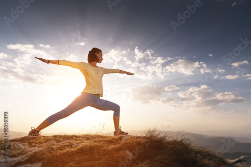 young woman practices yoga and fitness outdoors in a beautiful mountain landscape. Morning dawn, warrior pose