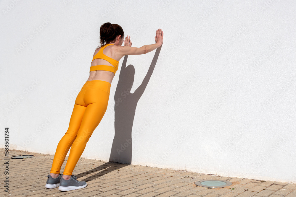 Sporty woman doing push off exercises against a wall