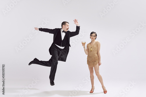 Retro man and attrative woman in vintage evening festive outfits entertaining, dancing over white background. Music, dance, vintage concept