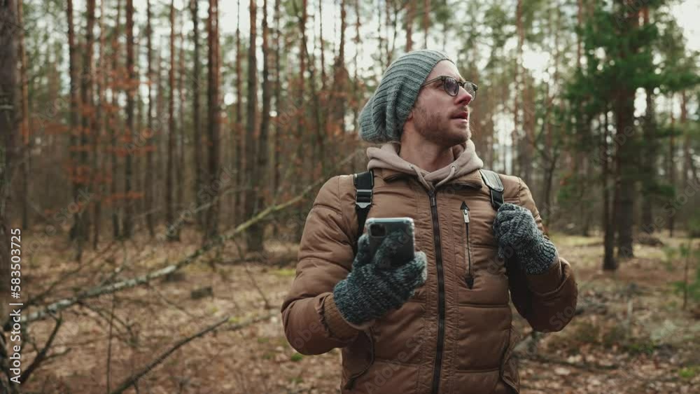 Serious tourist man in the hat looking for the way on the map on his mobile in the woods Serious tourist man in the hat looking for the way on the map on his mobile in the woods