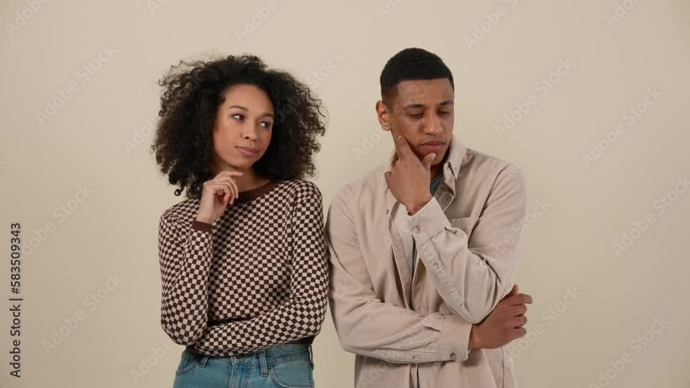 Pensive African young couple thinking and looking at the camera while standing in the beige studio Pensive African young couple thinking and looking at the camera while standing in the beige studio