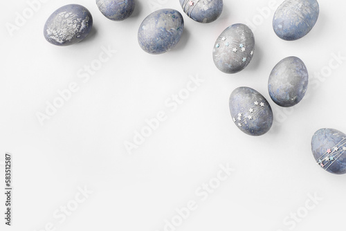 Festive Easter background. Gray-blue Easter eggs with stars on a white table. Greeting card with a place for text. Top view.