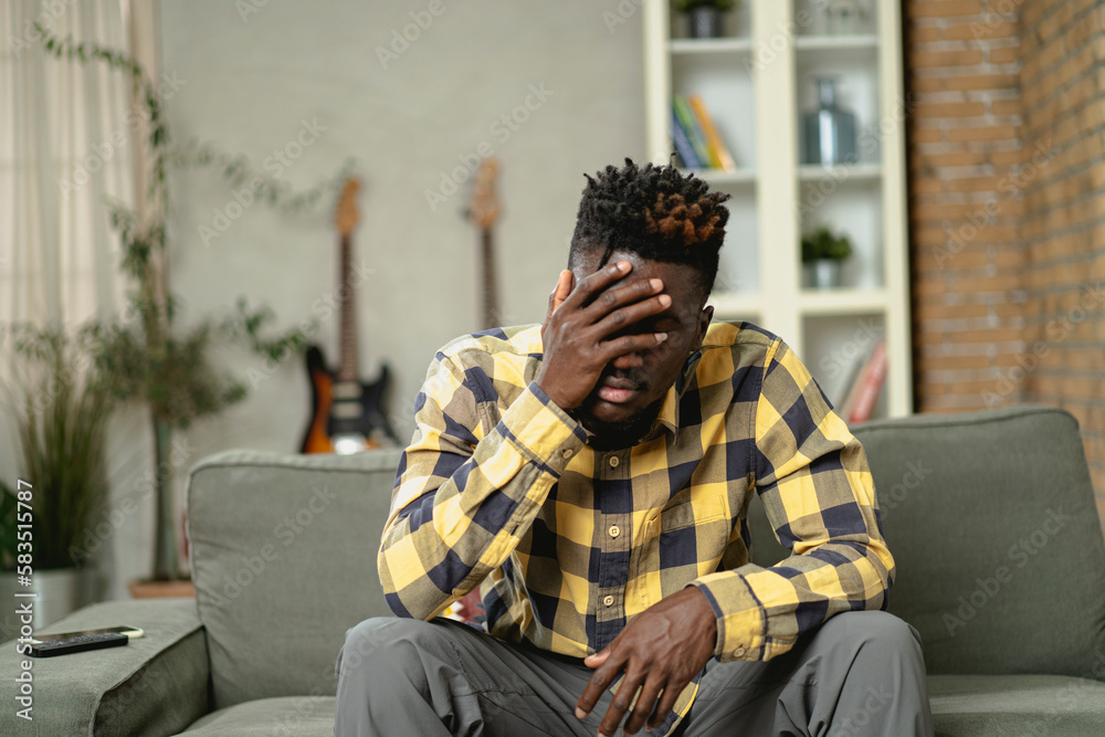 Sick man at home. Young African man sitting on sofa feeling unwell.