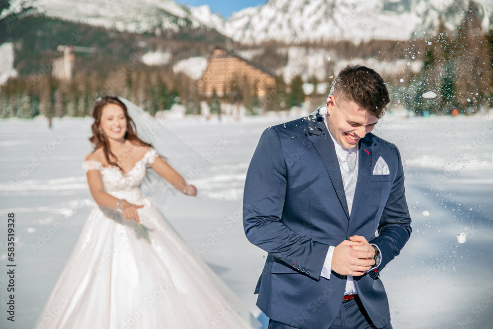 Young couple bride and groom playing in the winter nautre under snowy mountains on a frozen lake. playing snowball fight. throwing snow balls on each other. having a great time. laughing Young couple bride and groom playing in the winter nautre under snowy mountains on a frozen lake. playing snowball fight. throwing snow balls on each other. having a great time. laughing