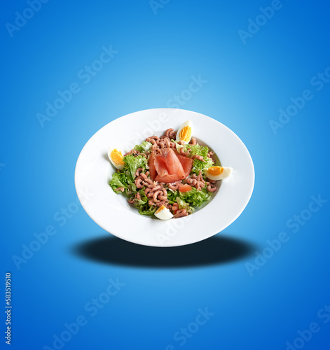 Floating White plate with shrimps and salmon on salad on blue gradient