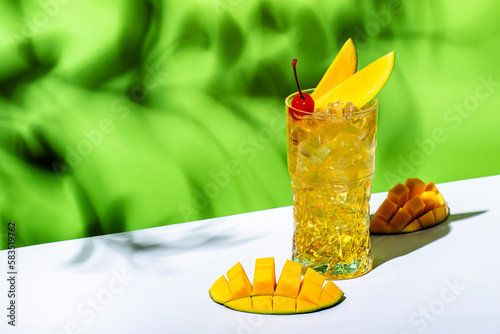Mango rum collins alcoholic cocktail drink with white rum, syrup, ginger beer, lemon juice, ice and mango. Green background,  copy space