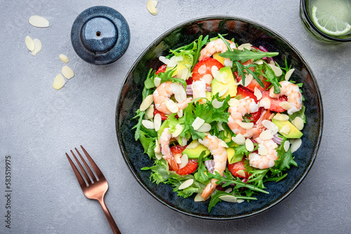 Strawberry, shrimp and herbs healthy salad with arugula, avocado and almond slices, gray kitchen table. Fresh useful dish for healthy eating