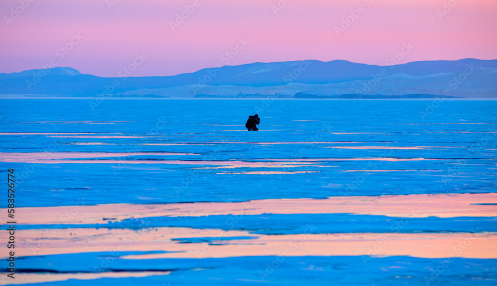 Fototapeta premium Photographer shoots a sunset among the snow-covered hummocks of Lake Baikal