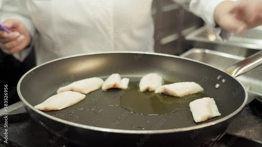 A chef pan-frying fish fillets for dinner to clients at a hotel. A chef pan-frying fish fillets for dinner to clients at a hotel.