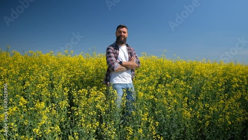 Happy and successful farmer is standing by his rapeseed field. Rapeseed plantation in bloom. Slow motion video.