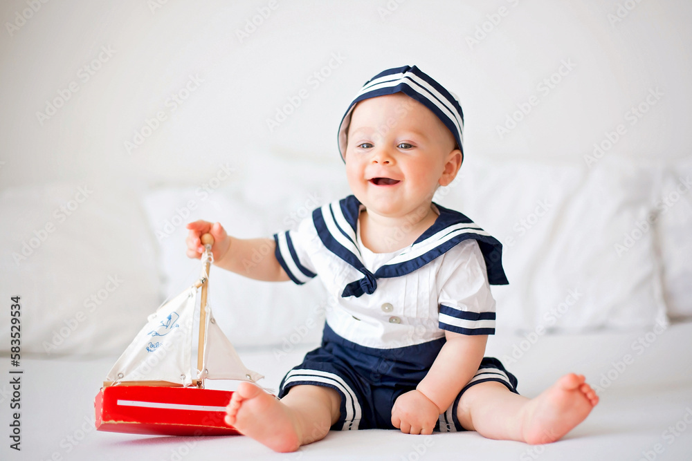 Cute baby boy, dressed in marine clothes, playing with wooden boat Cute baby boy, dressed in marine clothes, playing with wooden boat