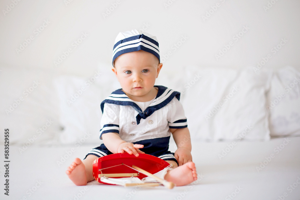Cute baby boy, dressed in marine clothes, playing with wooden boat Cute baby boy, dressed in marine clothes, playing with wooden boat