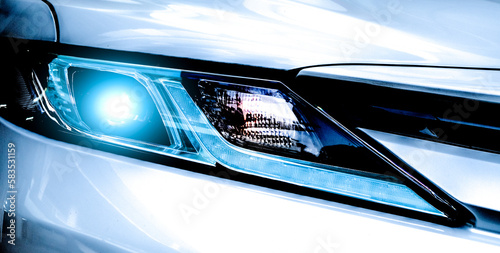Closeup headlamp light of a white luxury car. Automotive industry concept. Electric car or hybrid vehicle concept. Automobile leasing and insurance concept. Auto leasing business. Electric vehicle. © Artinun