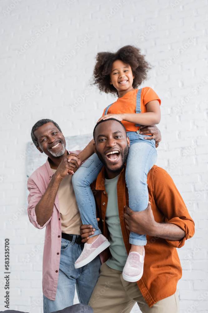 Cheerful african american man having fun with daughter and mature father at home.