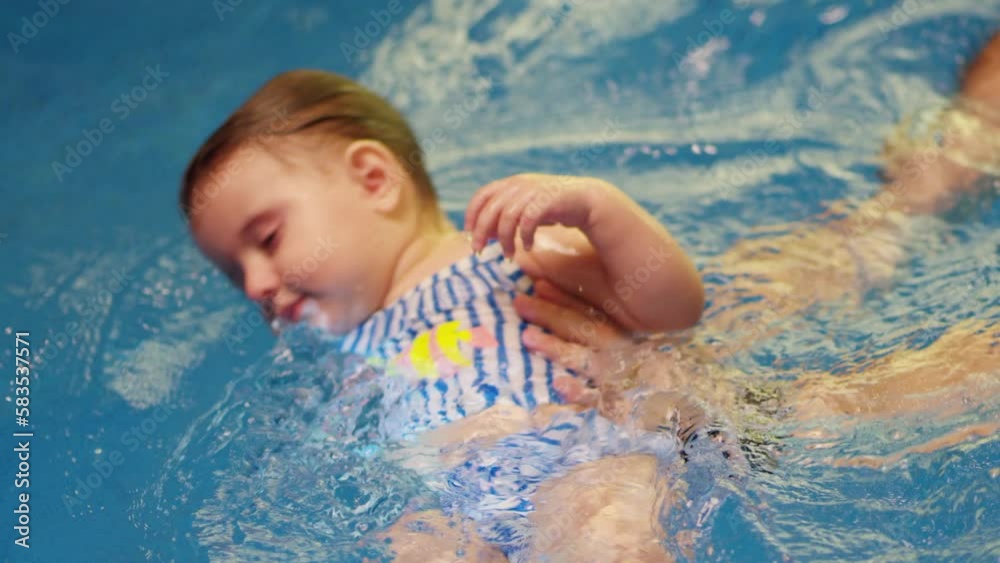 Father holding little baby and helping to swim in swimming pool with clean blue water. Professional water therapy for kids . Swimming training from an early age . Parent having fun . Happy lifestyle Father holding little baby and helping to swim in swimming pool with clean blue water. Professional water therapy for kids . Swimming training from an early age . Parent having fun . Happy lifestyle