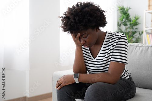 Sad african american woman sitting on sofa. Depression, anxiety and racism concept.