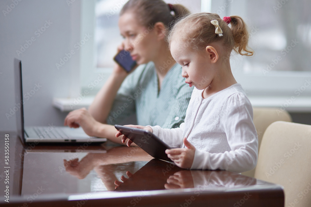 A girl is playing with a tablet. Stressed mother working attending a phone call and taking care of her baby at office A girl is playing with a tablet. Stressed mother working attending a phone call and taking care of her baby at office