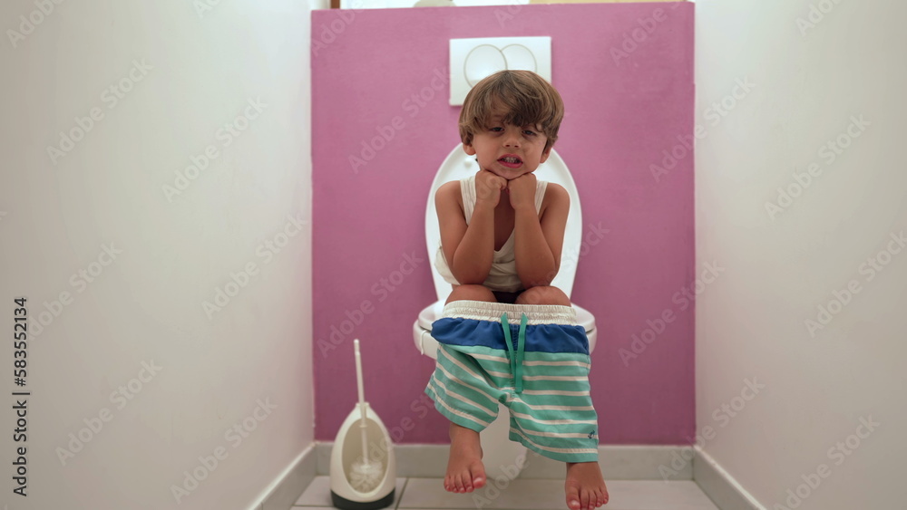 Obraz premium One cute small boy seated at toilet seat doing his needs at bathroom