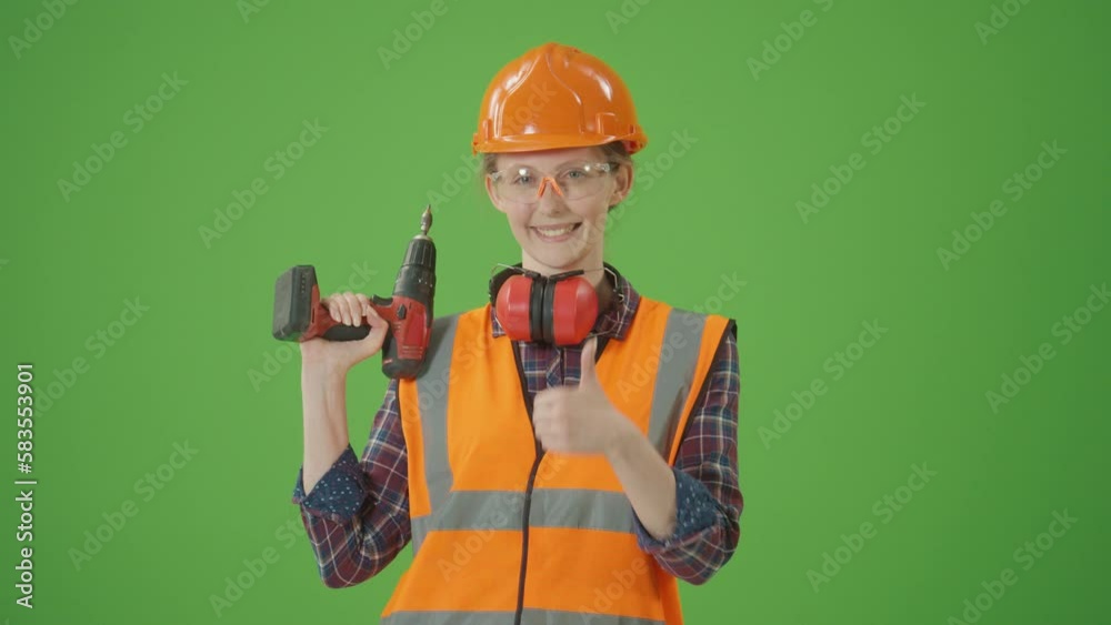 Green Screen.Young Female Construction Worker in Checkered Shirt,Safety Jacket,Helmet,Protective Glasses, Lifting the Drill Up,Smiling and Making Thumbs Up.Modern Construction , Happy Worker Concept. Green Screen.Young Female Construction Worker in Checkered Shirt,Safety Jacket,Helmet,Protective Glasses, Lifting the Drill Up,Smiling and Making Thumbs Up.Modern Construction , Happy Worker Concept.