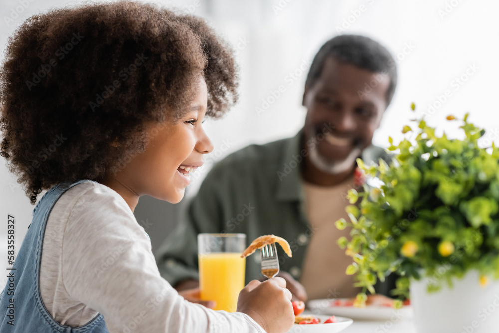 happy happy african american kid holding fork with pancake while having breakfast with grandfather. happy happy african american kid holding fork with pancake while having breakfast with grandfather.