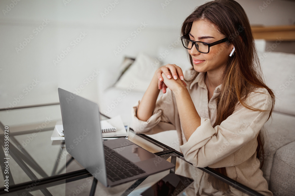Smiling millennial mixed race woman in wireless headphones and glasses has video call on laptop