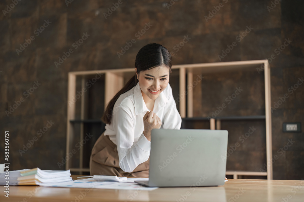 Excited young asian woman sitting at table with laptop and celebrating success Excited young asian woman sitting at table with laptop and celebrating success