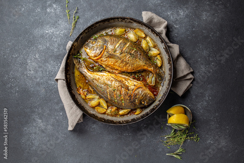 Baked sea bream or dorada with onion and herbs in pan on dark background