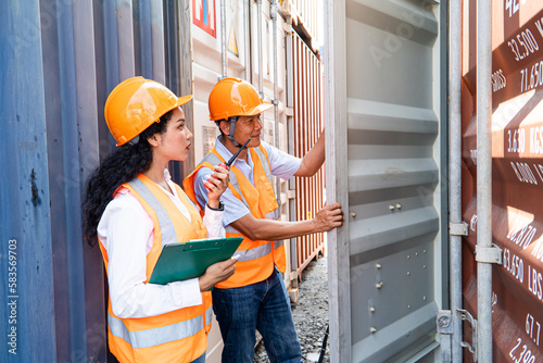 asian woman Engineer with note clipboard and asian man Supervisor in Hard Hats and Safety Vests Stand in Container Terminal. Container in export and import business and logistics.