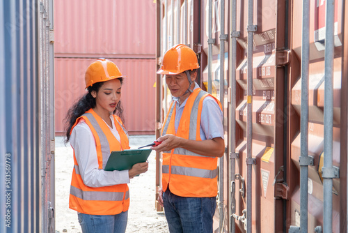 asian woman Engineer with note clipboard and asian man Supervisor in Hard Hats and Safety Vests Stand in Container Terminal. Container in export and import business and logistics.