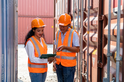 asian woman Engineer with note clipboard and asian man Supervisor in Hard Hats and Safety Vests Stand in Container Terminal. Container in export and import business and logistics.