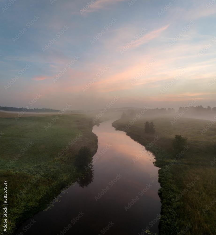 Aerial view of a foggy forest and calm river in the countryside during sunrise