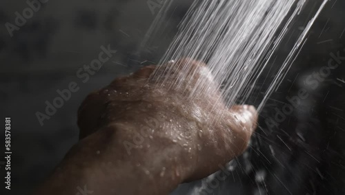 Water from the shower pours onto a man's hand in a stream, close-up