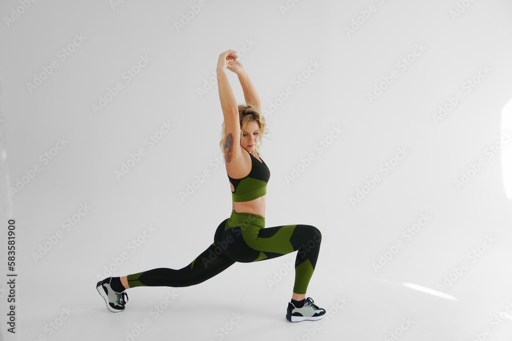 a blonde in a tracksuit makes stretching lunges on a white background