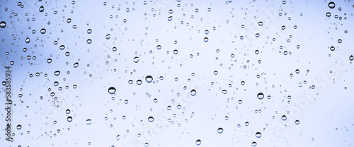 Minimal light backdrop with rain droplets on white glass. Light wet window with rainy drops closeup in blue light. Blurry minimalist monochrome background of window glass with raindrops close up.