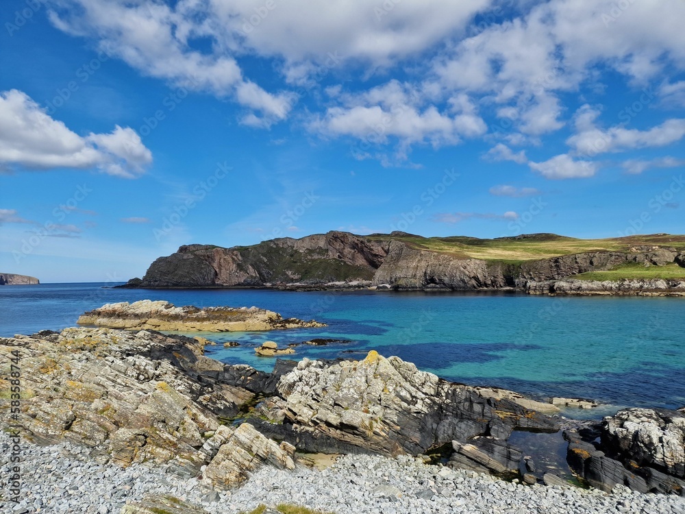 Landscape shot of a rocky coast of a lake surrounded by hills under the cloudy blue sky