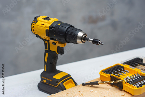 Electric cordless screwdriver on the battery on the table with a self-tapping screw in the board.