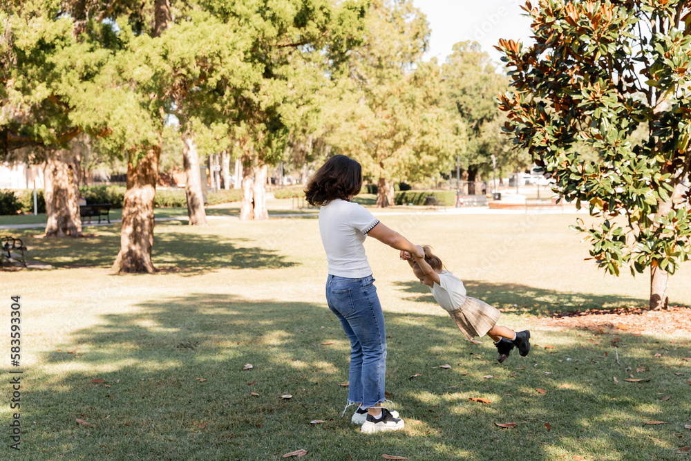 full length of brunette mother in jeans playing with toddler daughter in park of Miami.