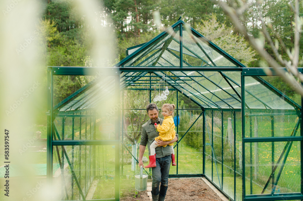 Father holding his little daughter in feco greenhouse,taking care of vegetable together, sustainable lifestyle.
