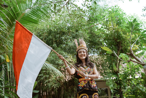 asian woman in king bibinge waving the indonesian flag and smiling while standing at the nature photo