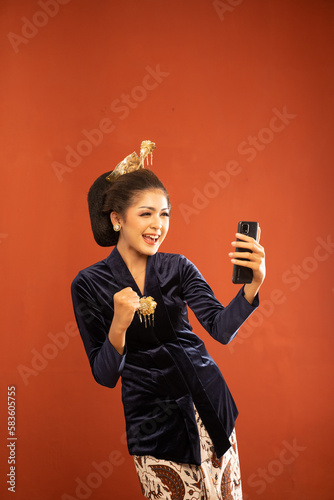 asian woman in bludru kebaya standing looking at the phone and clenched her hand on isolated background photo